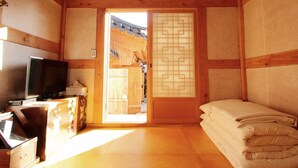 A traditional Japanese room with tatami flooring, a sliding door with a geometric pattern, a television on a wooden cabinet, and a bed with neatly folded bedding. - Doldam House (Jeonju)