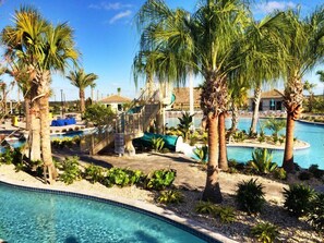 Zona de piscina con palmeras, una escalera y un edificio al fondo.