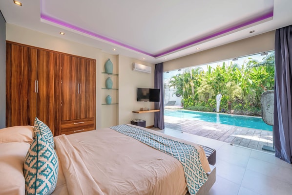 A bedroom with a large bed, a TV, a wardrobe, and a view of a swimming pool. - Villa Sawah (Seminyak)