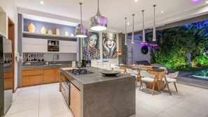 A modern kitchen with a central island, pendant lighting, and a dining area with chairs and a table. - Villa Sawah (Seminyak)