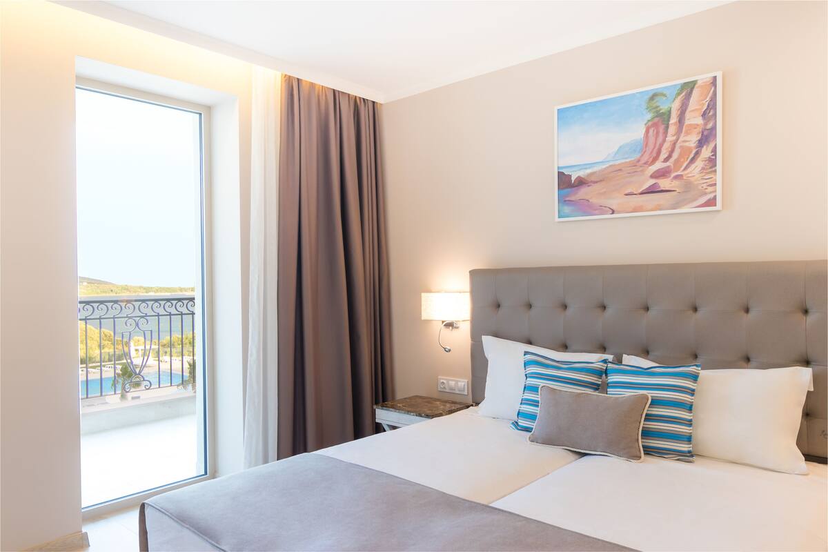 Habitación de hotel con una cama grande, vistas a un balcón con piscina y un cuadro en la pared.