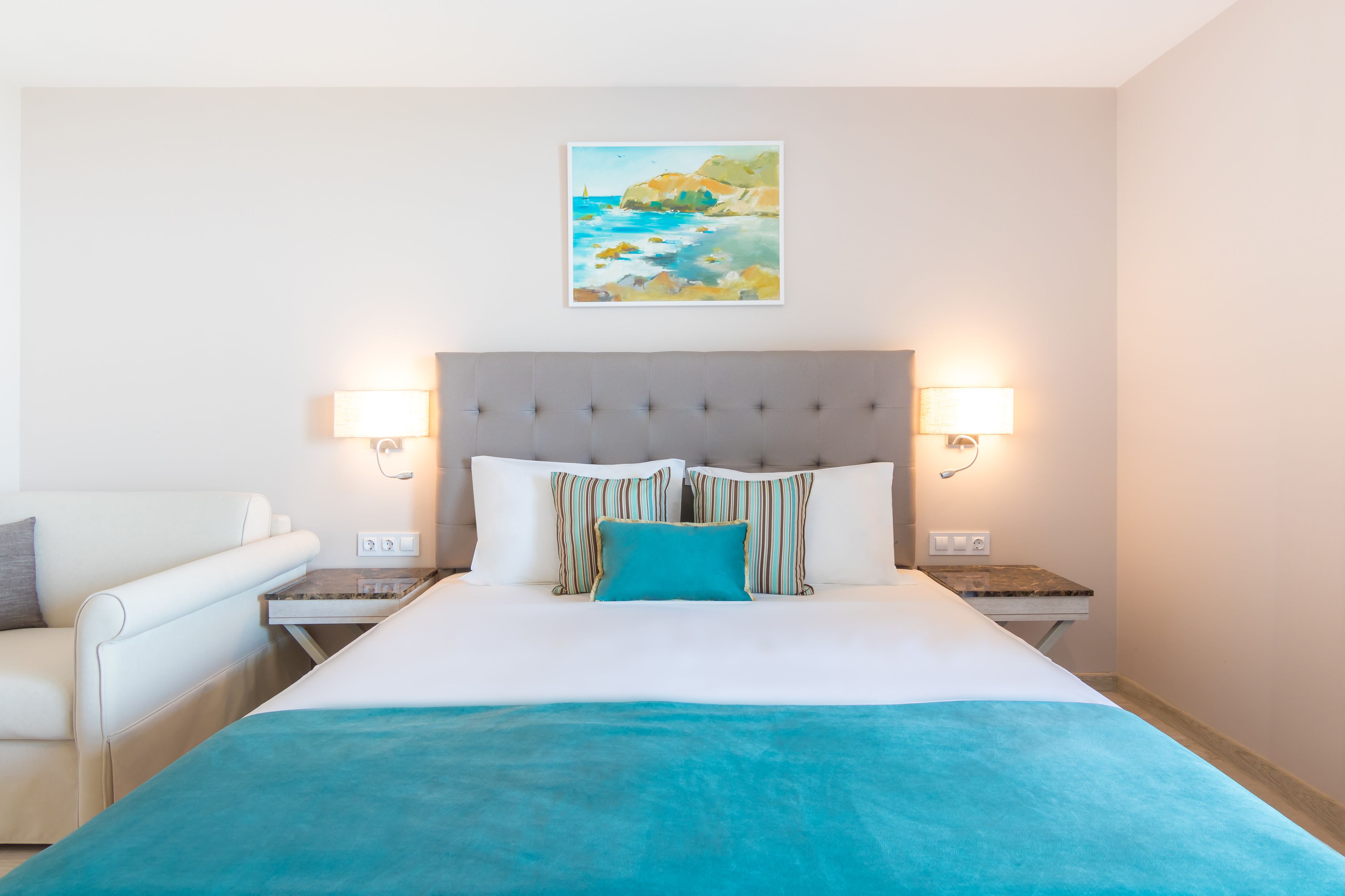 Een hotelkamer met een groot bed, een hoofdeinde, twee bedlampjes, een schilderij aan de muur en een klein tafeltje.