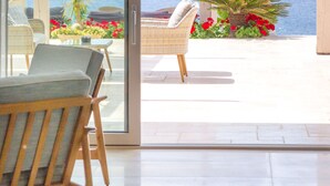 A modern room with a large sliding glass door leading to a balcony with a view of the sea. There are wicker chairs and a small table with flowers on the balcony. - King Maron Beach Hotel & Spa (Maroneia-Sapes)