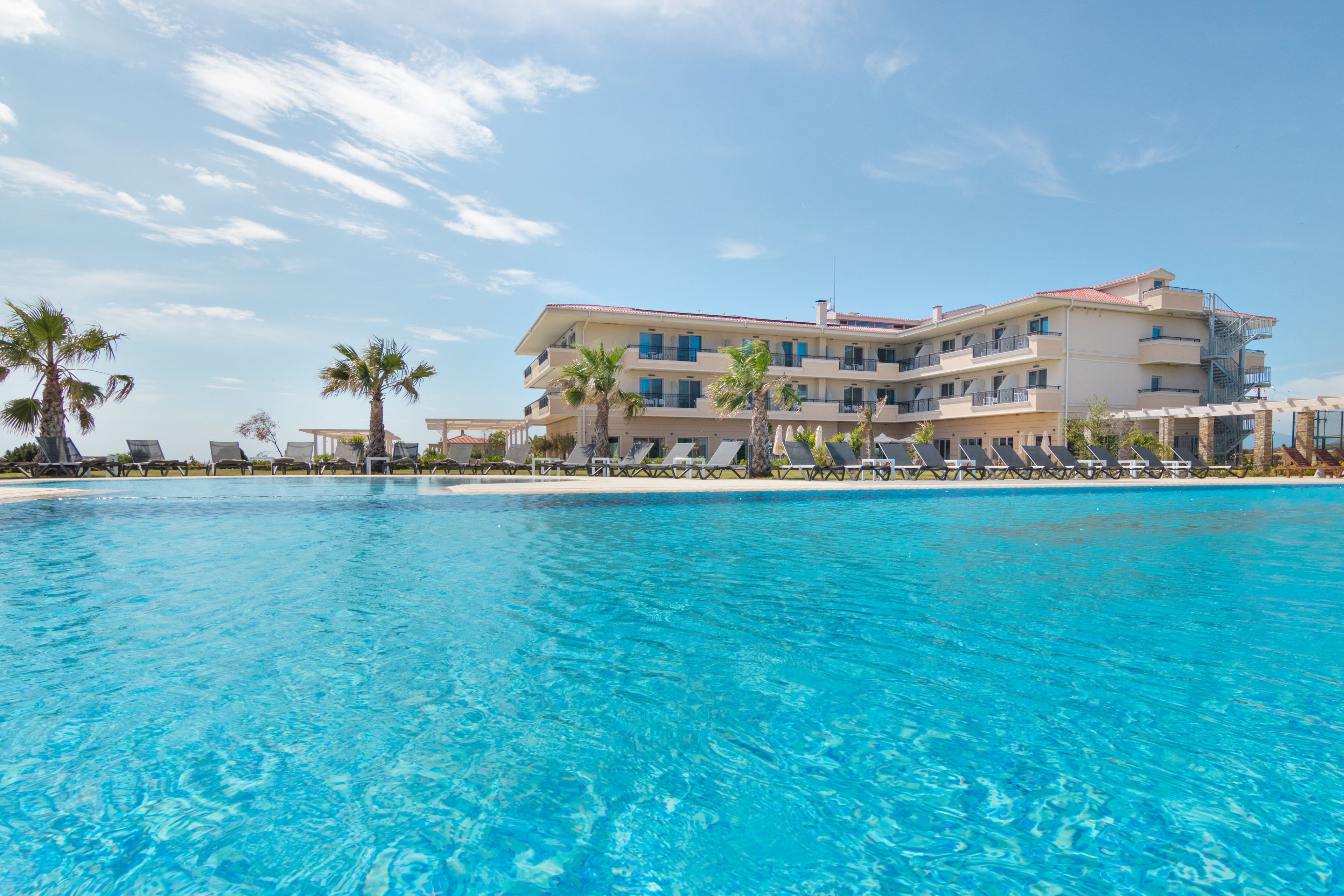 A hotel with a pool, palm trees, and a clear blue sky.