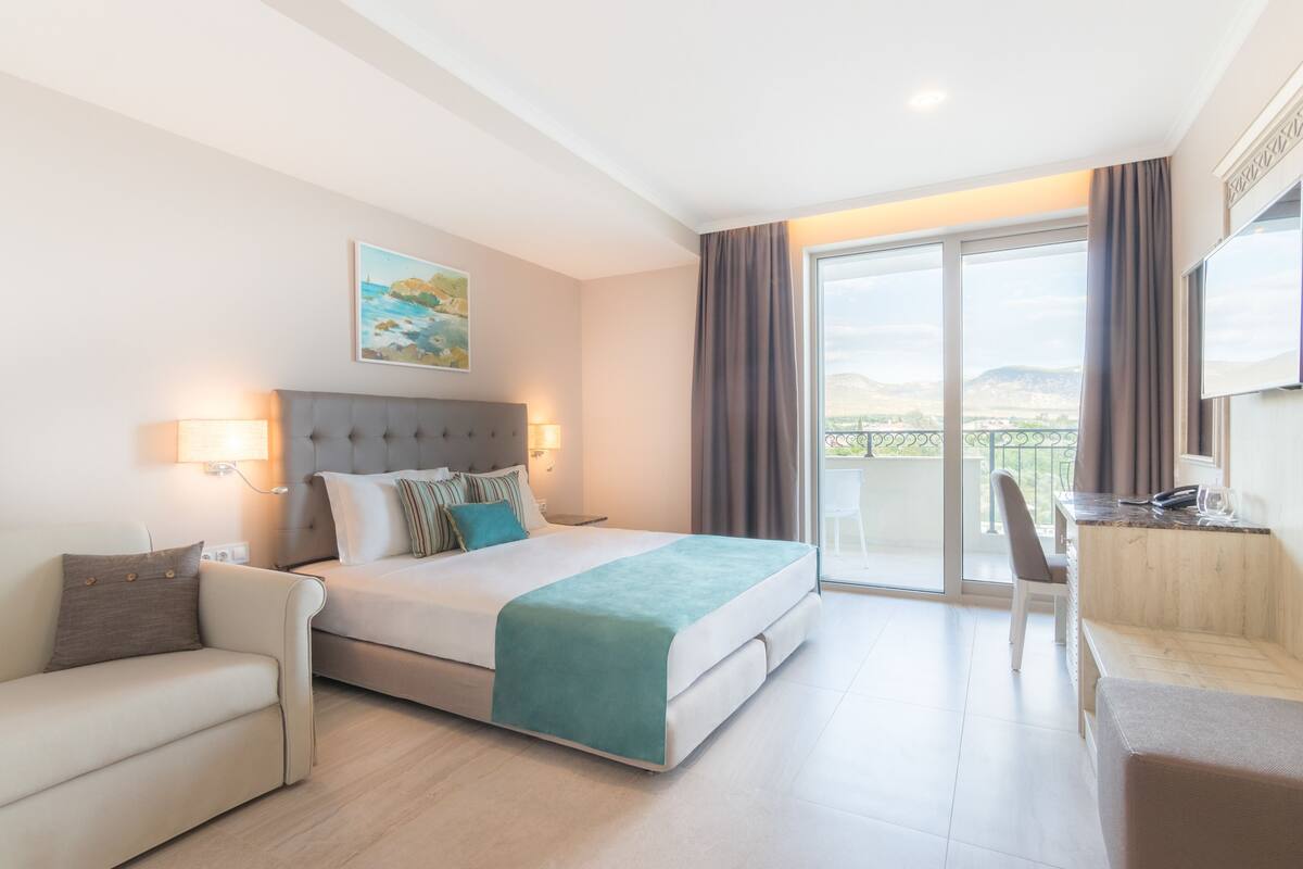 Habitación de hotel con cama, escritorio, silla y balcón con vistas.