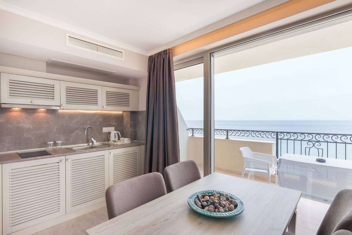 Una cocina moderna con vistas al mar, un área de comedor con mesa y sillas, y un balcón con barandilla.