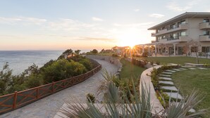 A coastal hotel with a paved walkway, a view of the sea, and a building with balconies. - King Maron Beach Hotel & Spa (Maroneia-Sapes)