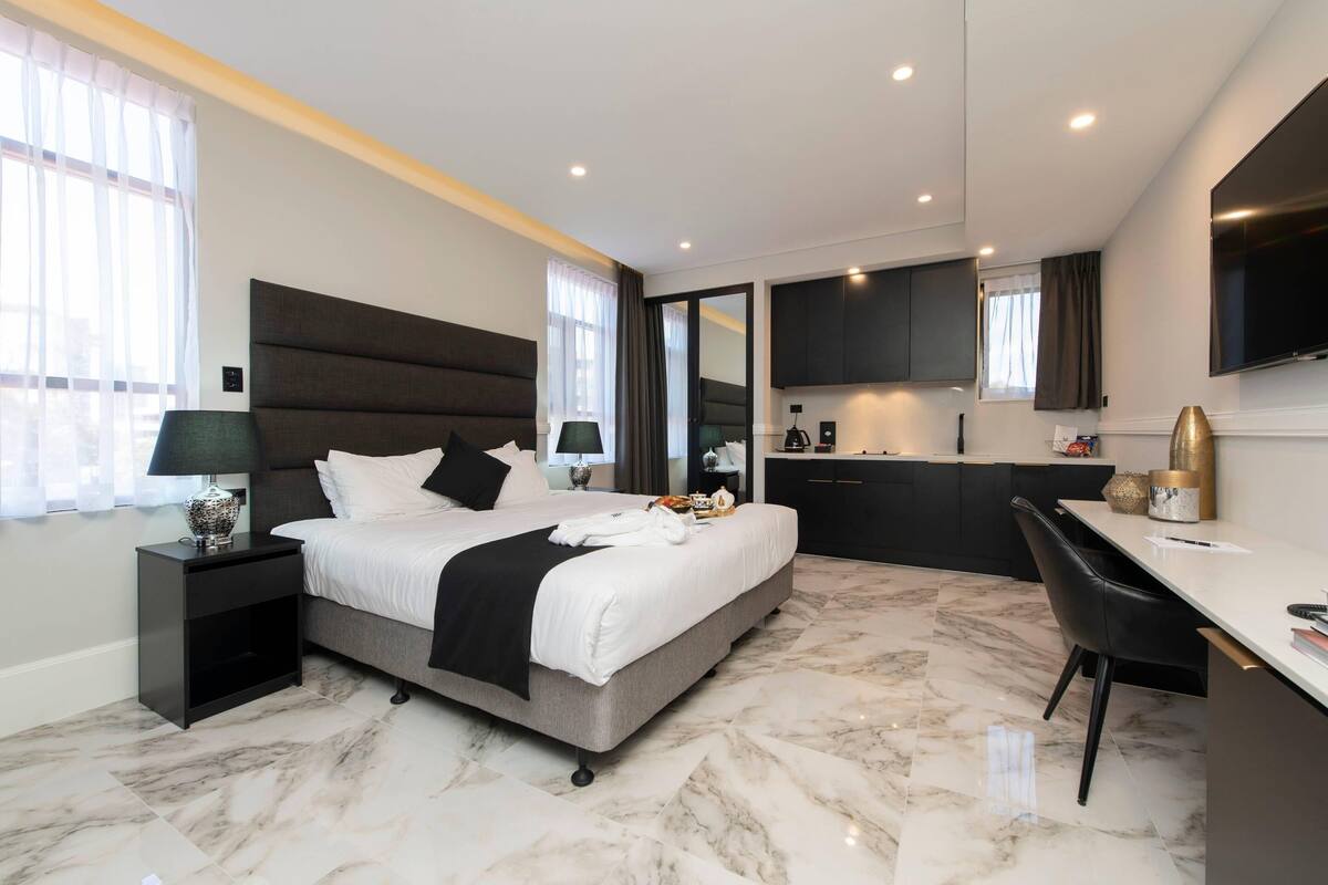 A modern bedroom with a large bed, bedside tables, a desk, and a flat-screen TV.