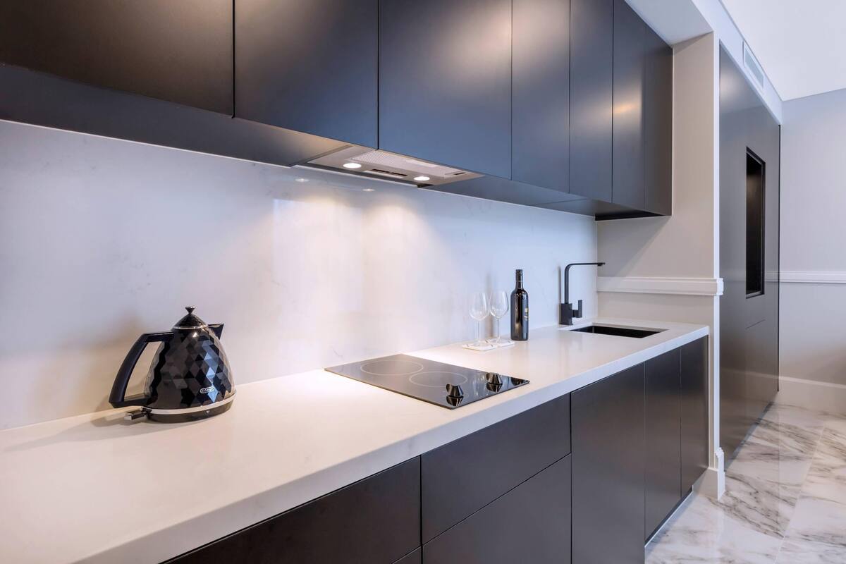 A modern kitchen with dark cabinetry, a white countertop, and a built-in stove.