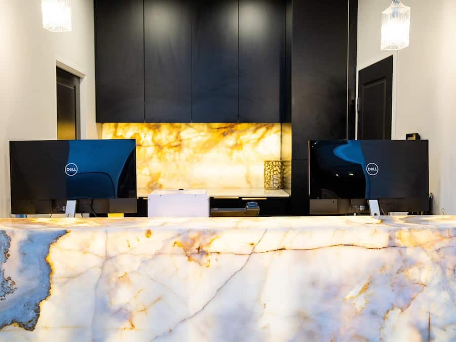 Una mesa de recepción con dos computadoras Dell, una encimera de mármol y armarios negros.