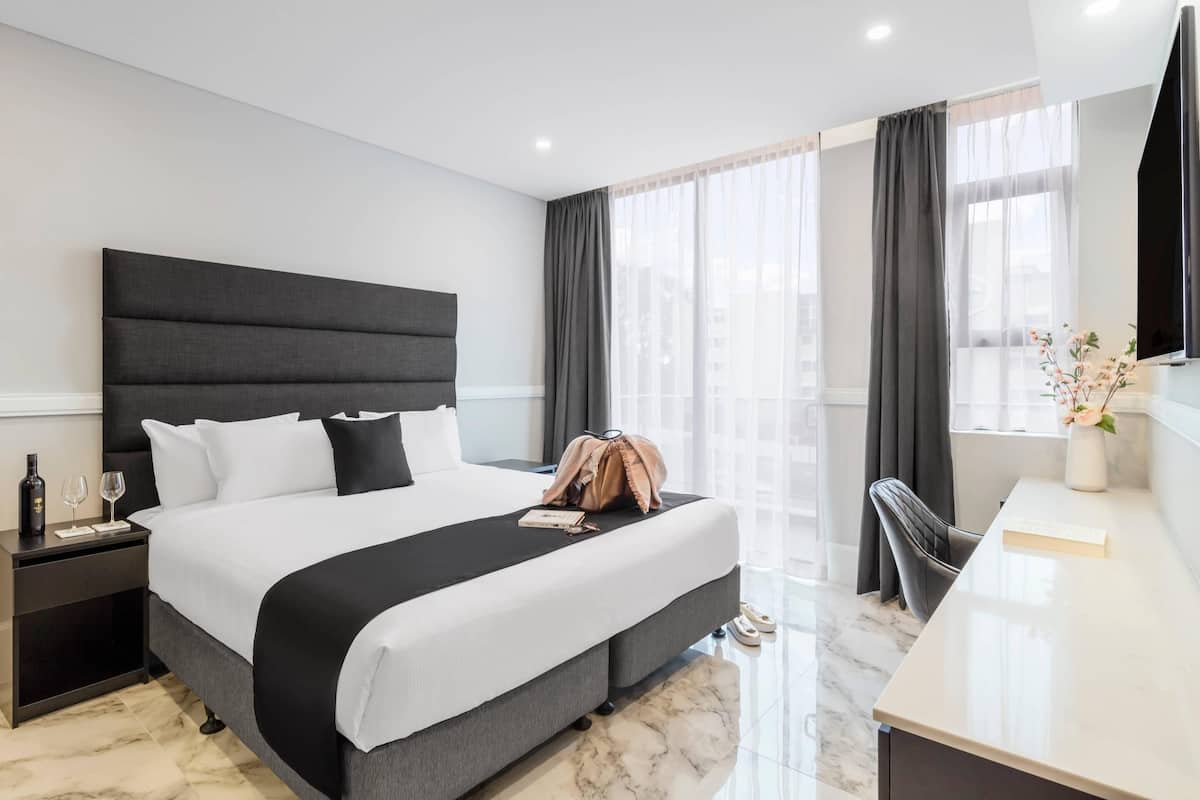 A modern hotel room with a large bed, a desk, and a view of the city.