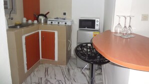 A compact kitchen with a stove, microwave, and a small dining table with chairs. - Residence 2 Pièces Duplex (Abidjan)