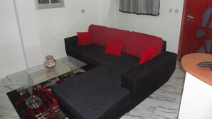 A living room with a black and red sofa, a glass coffee table, and a small window. - Residence 2 Pièces Duplex (Abidjan)