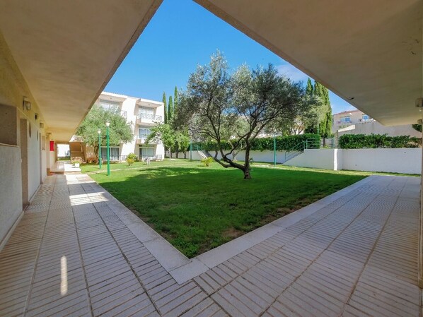 Un patio con suelo de baldosas, césped y un árbol.