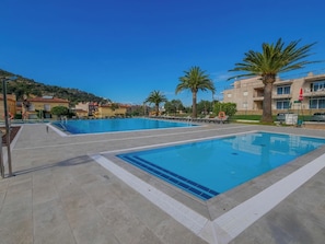 A swimming pool area with multiple pools, palm trees, and a building in the background.