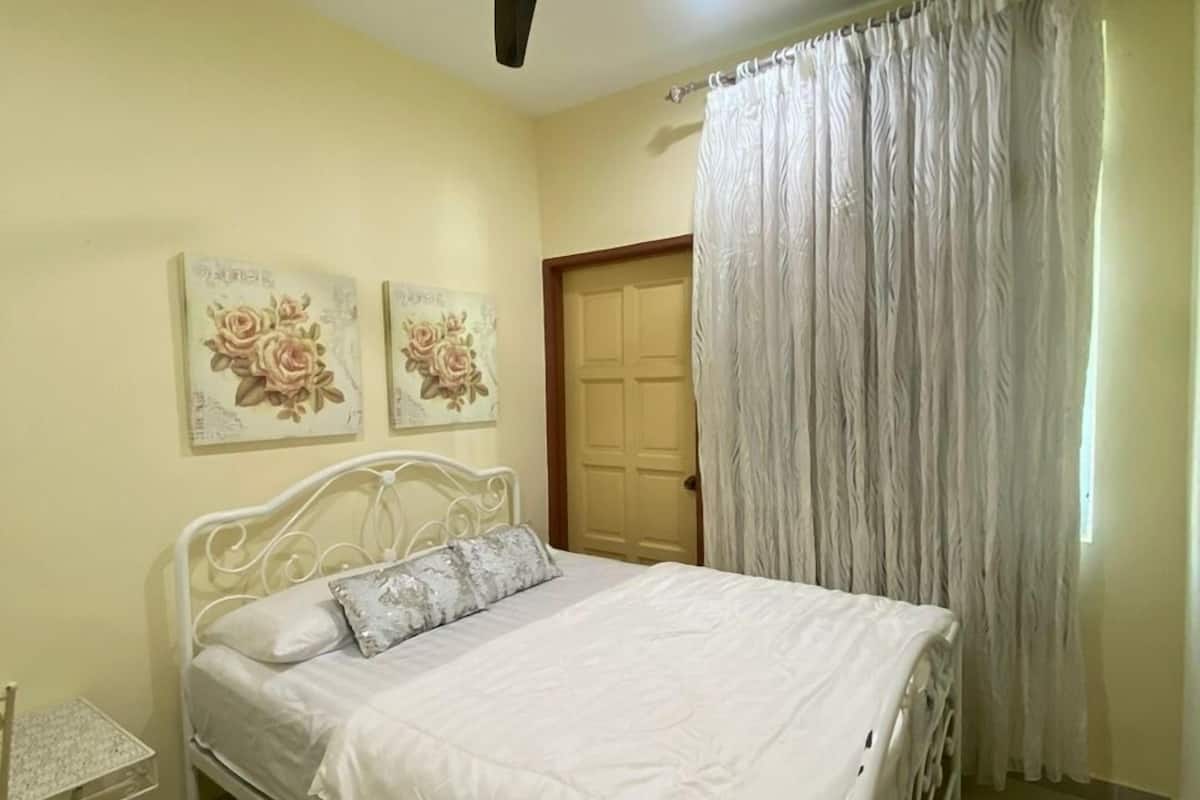 A bedroom with a bed, a ceiling fan, a door, and a window with curtains.