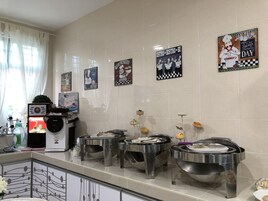 Un área de cocina con cafetera, ollas de acero inoxidable y diversos alimentos a la vista.