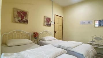 A room with two single beds, a ceiling fan, a door, and two wall-mounted paintings.