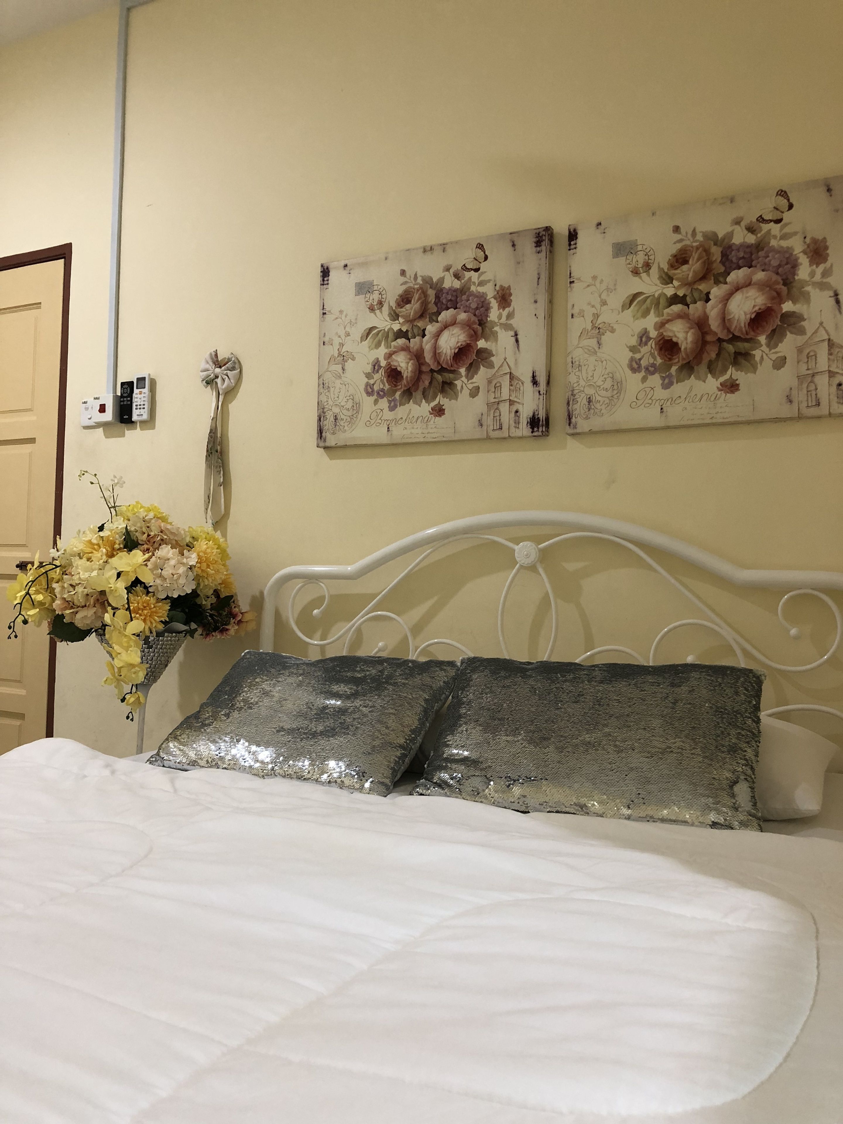 Een net opgemaakt bed met twee kussens, decoratieve bloemen behang en een vaas met bloemen.