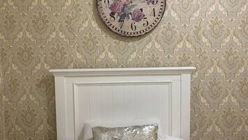 Una cama con cabecera blanca y un reloj decorativo con diseño floral en la pared superior.
