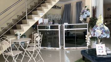 A modern hotel lobby with a staircase, a reception desk, and a seating area with chairs and a table.