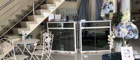 A modern hotel lobby with a staircase, a reception desk, and a seating area with chairs and a table.