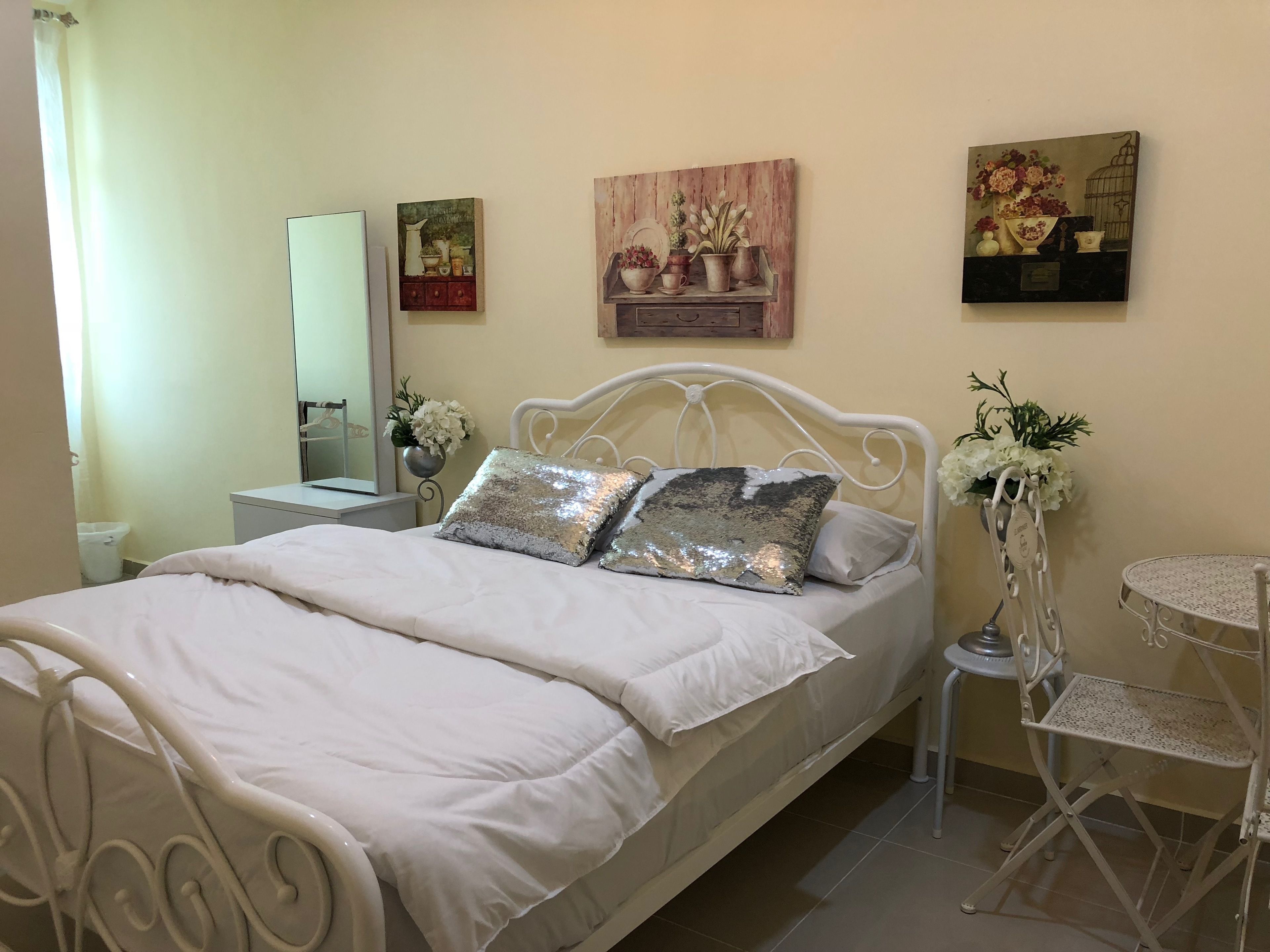 A neatly arranged bedroom with a bed, a bedside table, a mirror, and wall art.