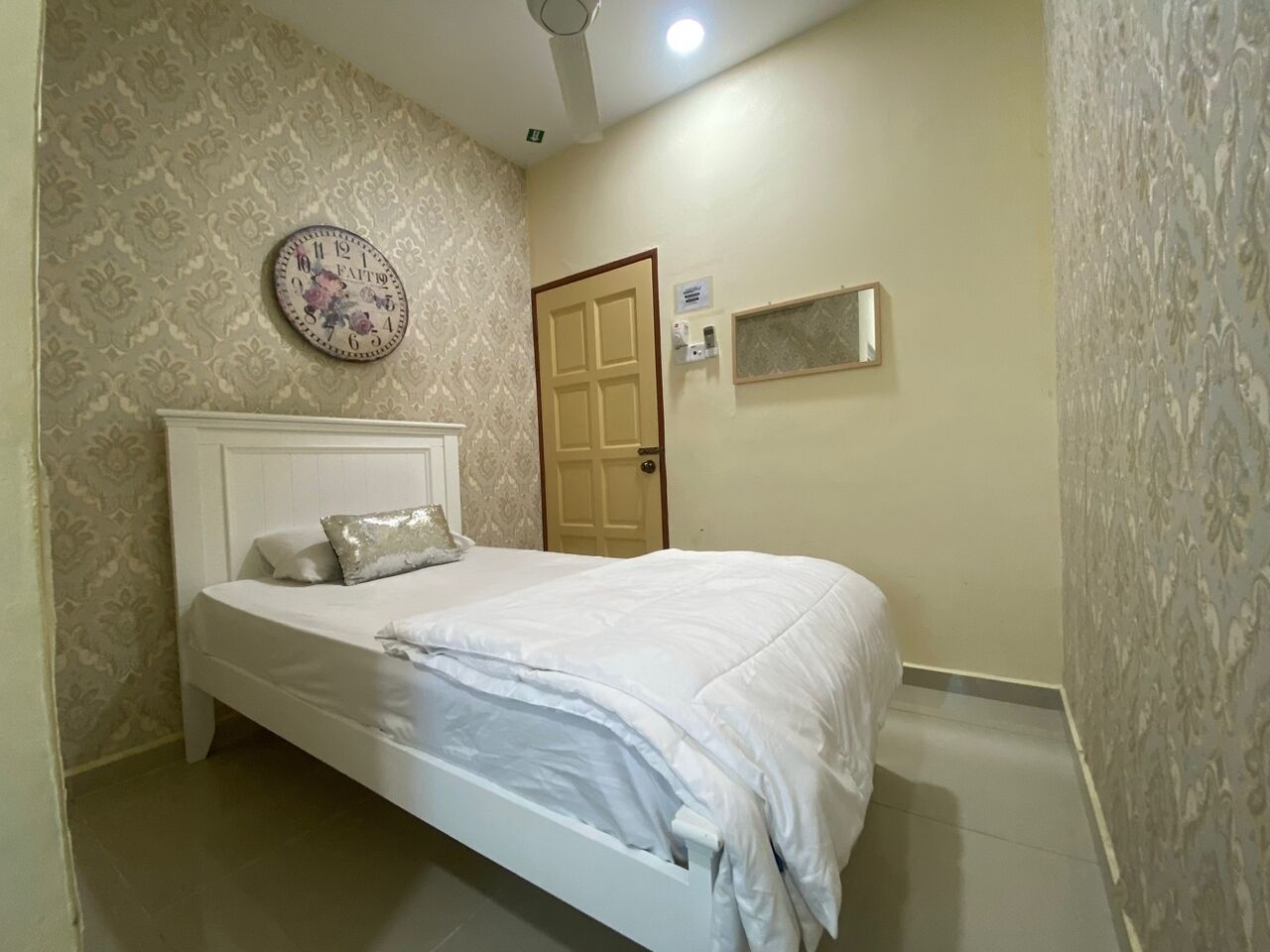 A bedroom with a bed, a wall clock, a door, and a small window.