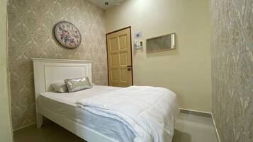 A bedroom with a bed, a wall clock, a door, and a small window.