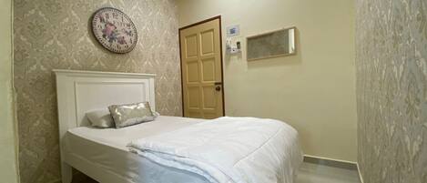A bedroom with a bed, a wall clock, a door, and a small window.