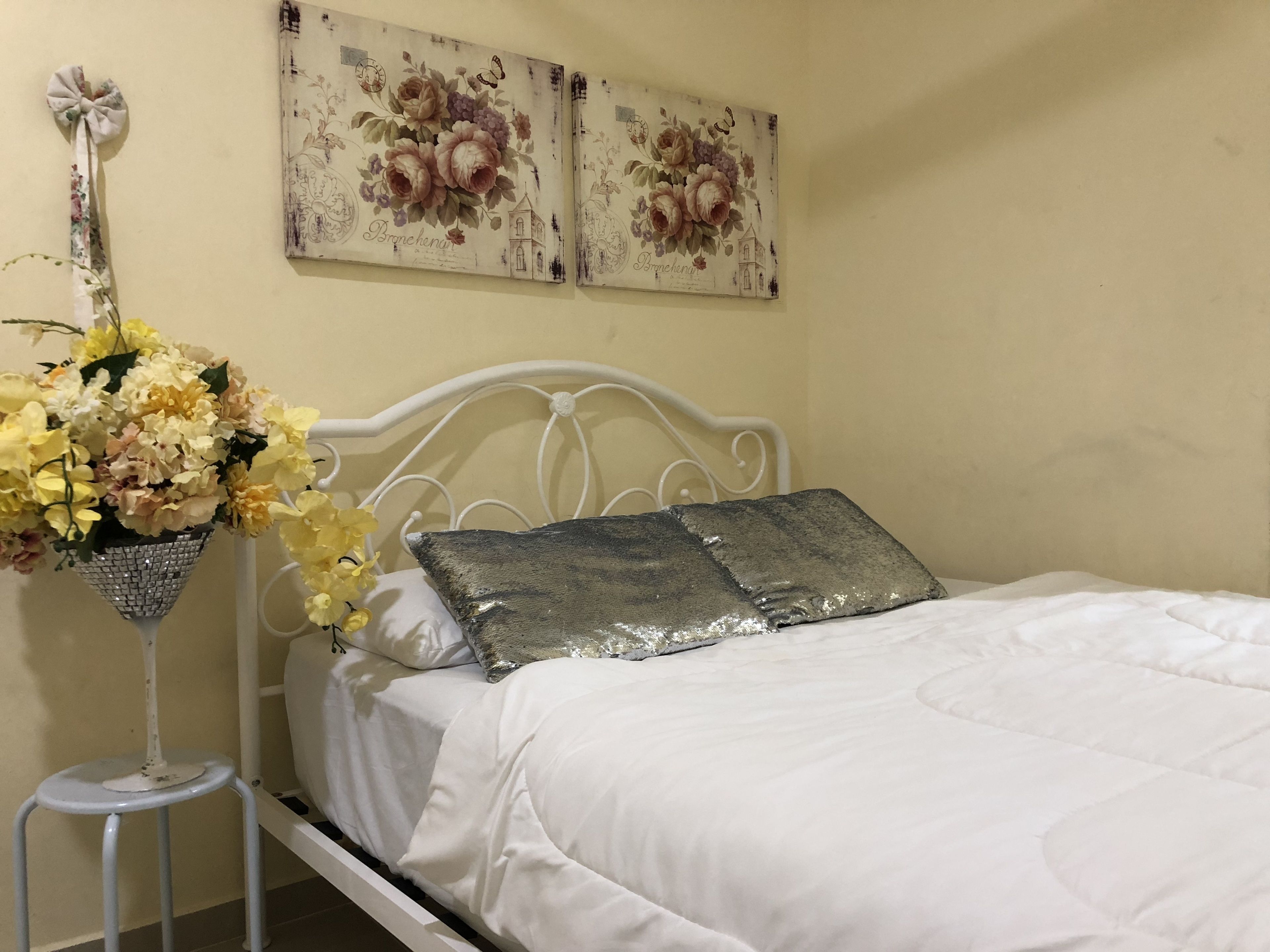 A bed with white bedding, a decorative pillow, and a floral arrangement on a side table.
