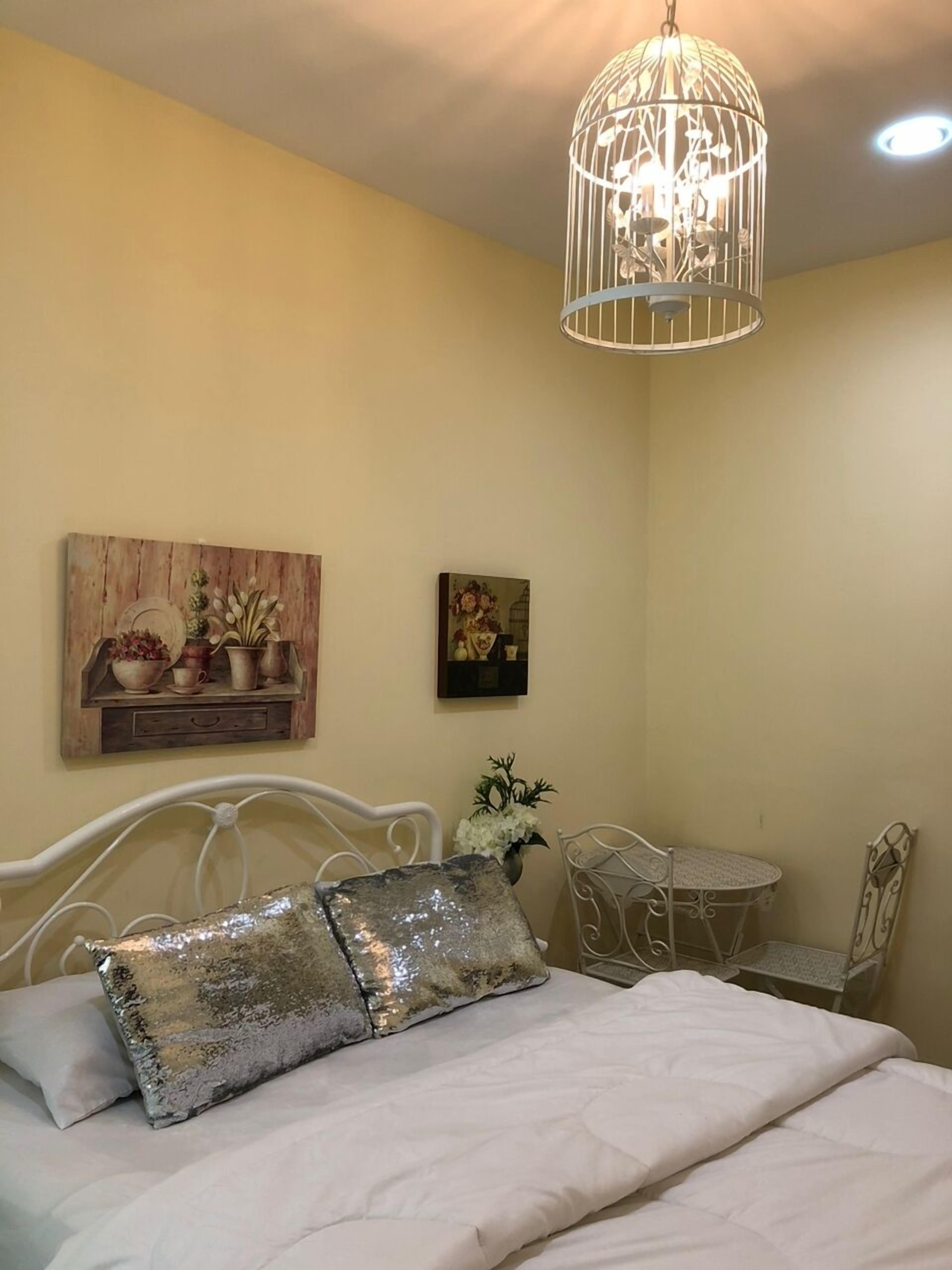 Un dormitorio con una cama, una mesita redonda pequeña, una silla, una lámpara colgante y adornos en la pared.