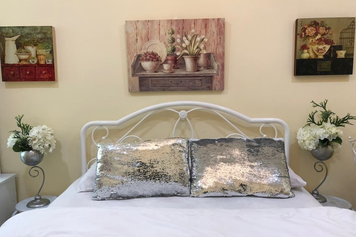 A bed with two large decorative pillows, a white metal headboard, and two bedside tables with small potted plants.