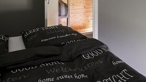 A bedroom with a sloped ceiling, a bed with black bedding, a wooden headboard, and a white wall-mounted coat rack.