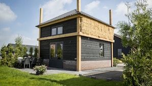 A modern two-story house with a dark wooden exterior, a thatched roof, and a chimney.