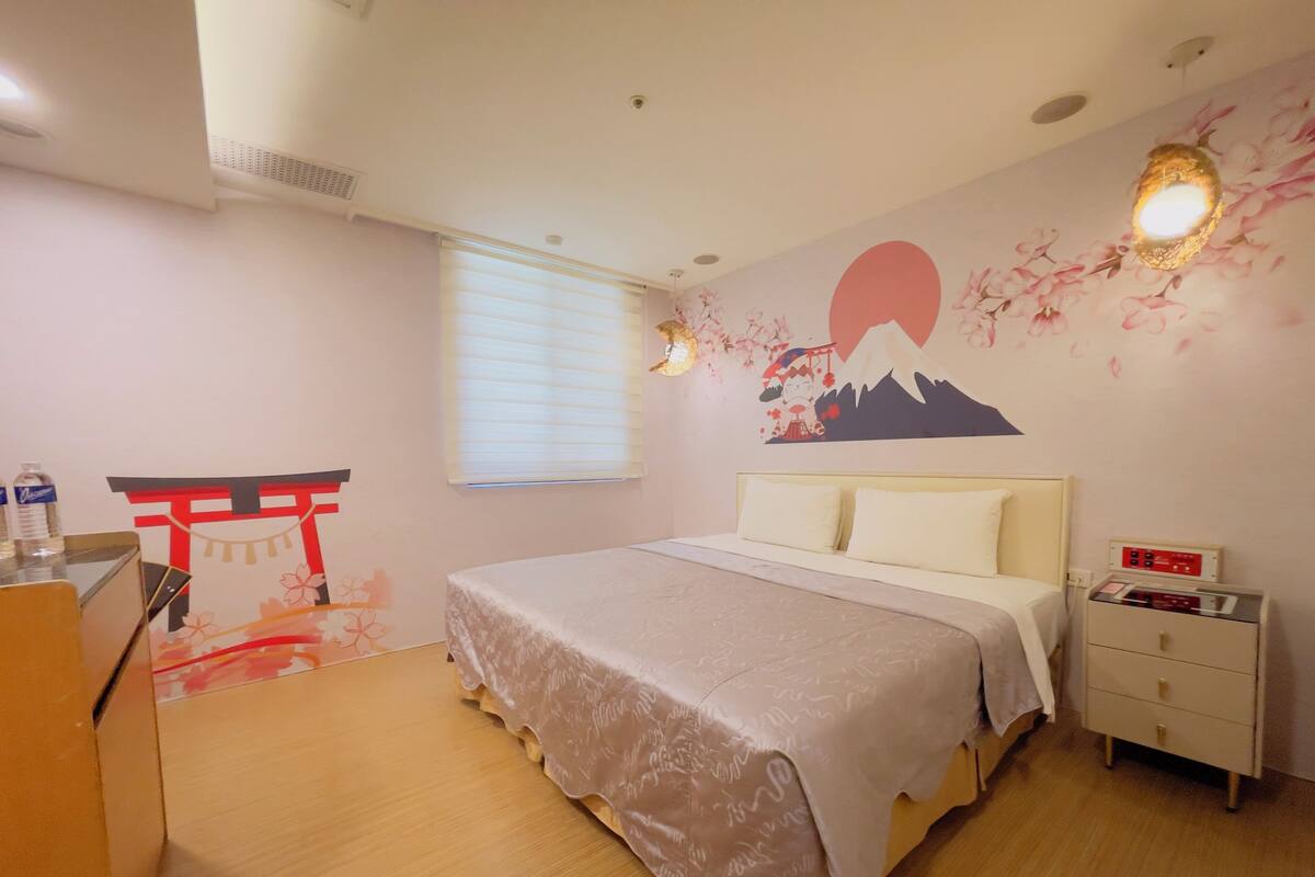 A bedroom with a bed, a nightstand, a wall-mounted shelf, a window with blinds, and a decorative wall mural.