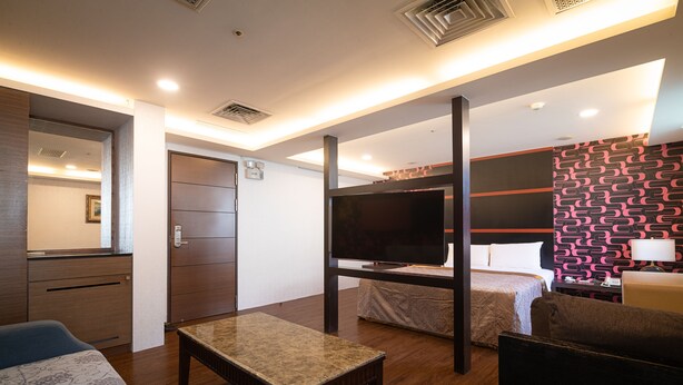 Quarto de hotel com cama, televisão, escrivaninha e sofá.