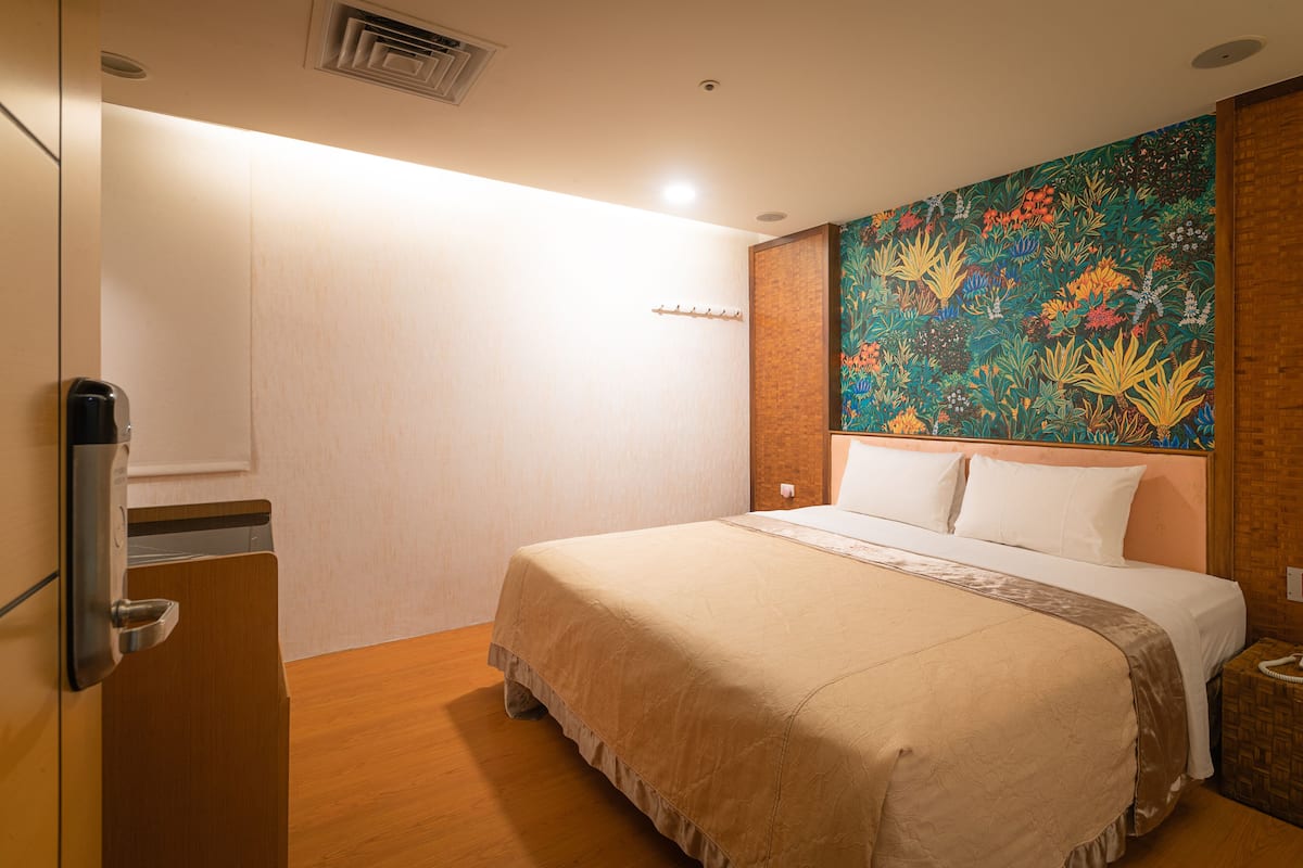 A hotel room with a large bed, a wooden wardrobe, a wall-mounted heater, and a colorful floral mural.