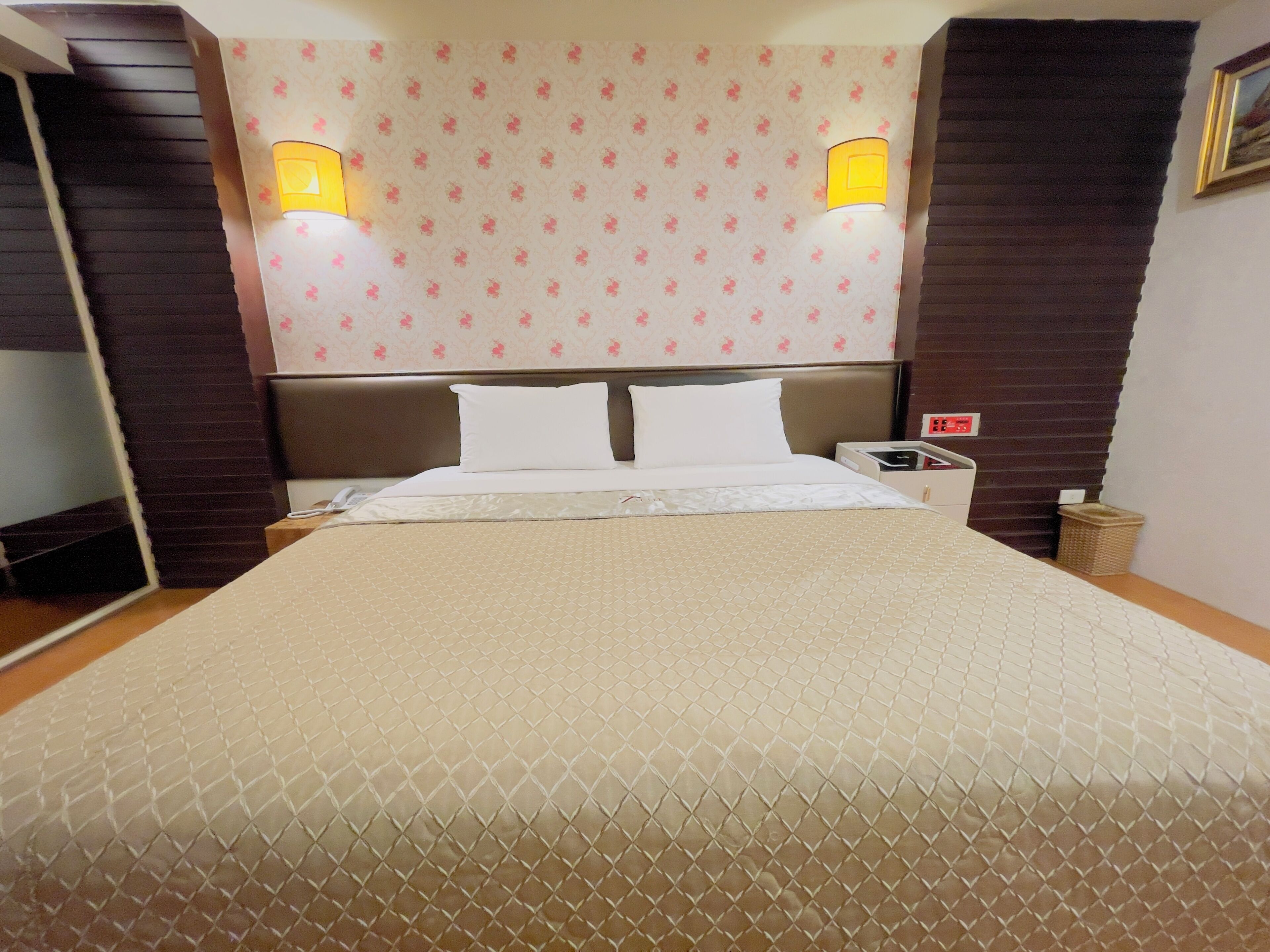 Una habitación de hotel con una cama grande, dos lámparas de noche, una mesita de noche y un reloj de pared.