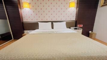 Una habitación de hotel con una cama grande, dos lámparas de noche, una mesita de noche y un reloj de pared.