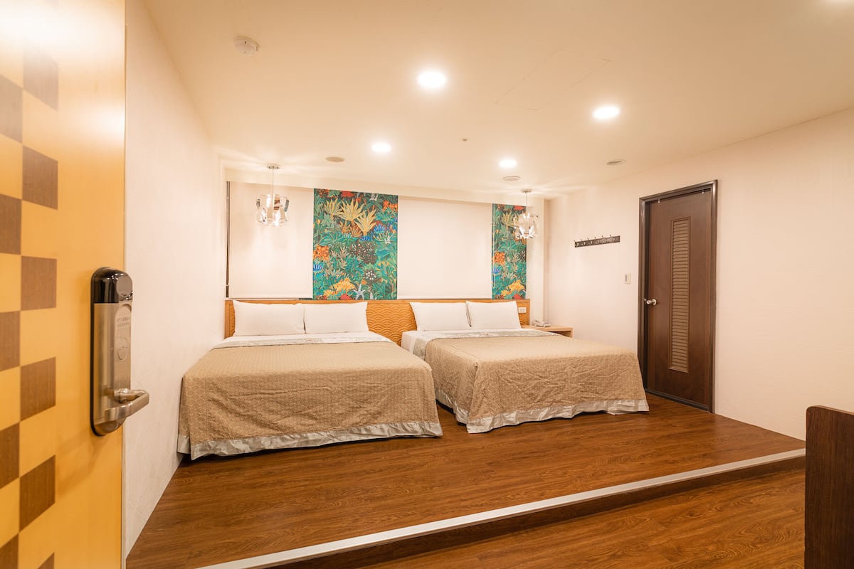 A hotel room with two beds, wooden flooring, and a large window with a view.