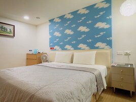 Un dormitorio con cama, mesita de noche, ventilador de pared y toma de corriente.