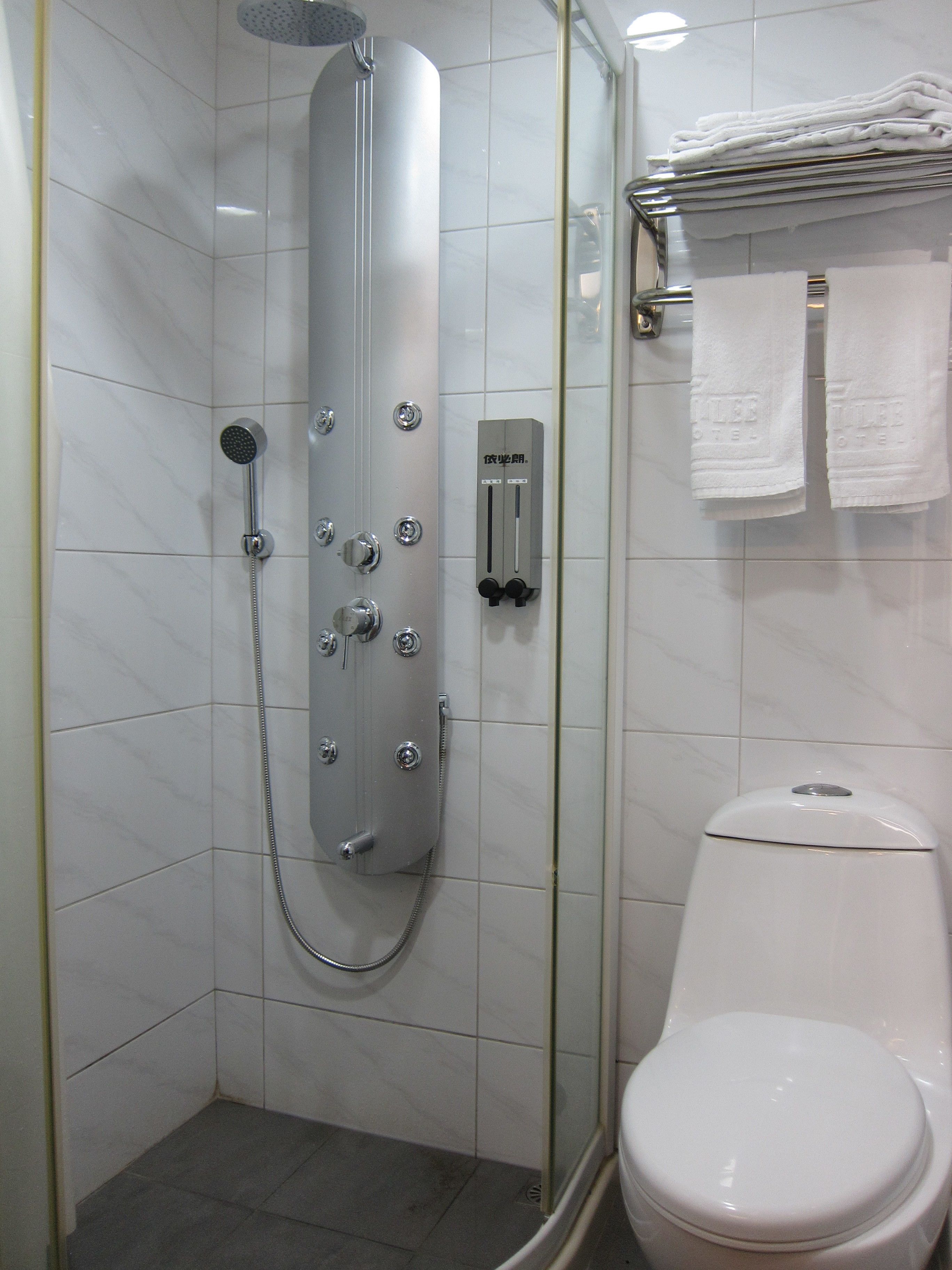 A modern bathroom with a glass-enclosed shower, a toilet, and a towel rack with folded towels.
