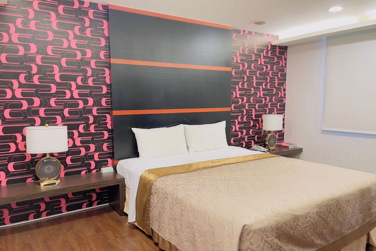 A hotel room with a bed, bedside tables, a lamp, and a patterned wall.