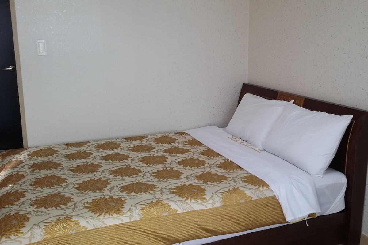 Ein Einzelbett mit einem blumigen Überwurf und weißen Kissen in einem Raum mit schlichten Wänden und einer Tür.
