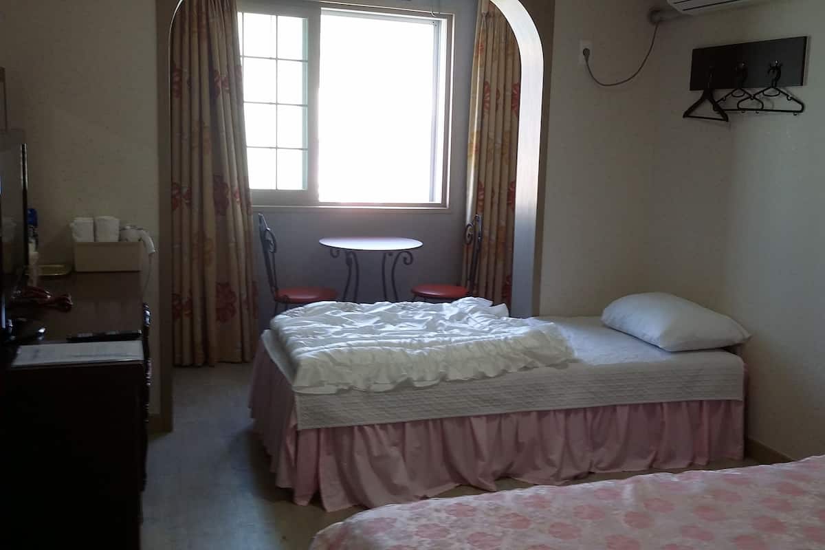Ein kleines, ordentlich eingerichtetes Schlafzimmer mit einem Einzelbett, einem Nachttisch, einem Stuhl und einem kleinen Tisch.