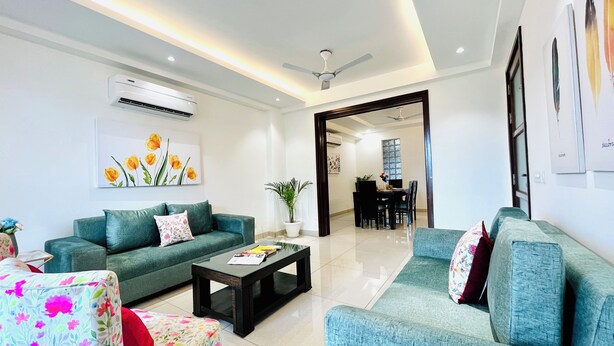 Una sala de estar moderna con sofás color turquesa, una mesa de centro y un comedor al fondo.