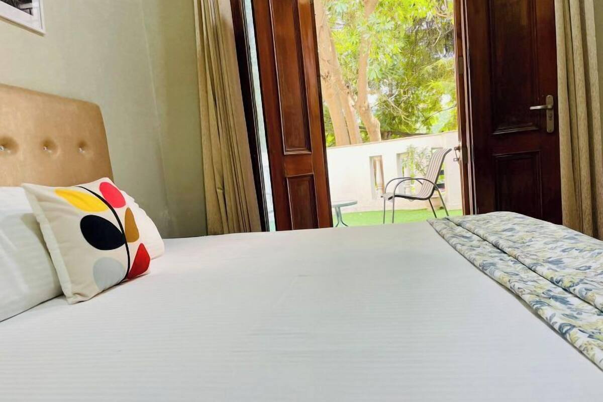 Un dormitorio con cama, almohada estampada con lunares, puerta de madera y vista a un jardín exterior.