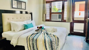 Una cama bien hecha con sábanas blancas, una colcha a rayas y un cojín azul verdoso. Hay dos cuadros enmarcados en la pared sobre la cama.