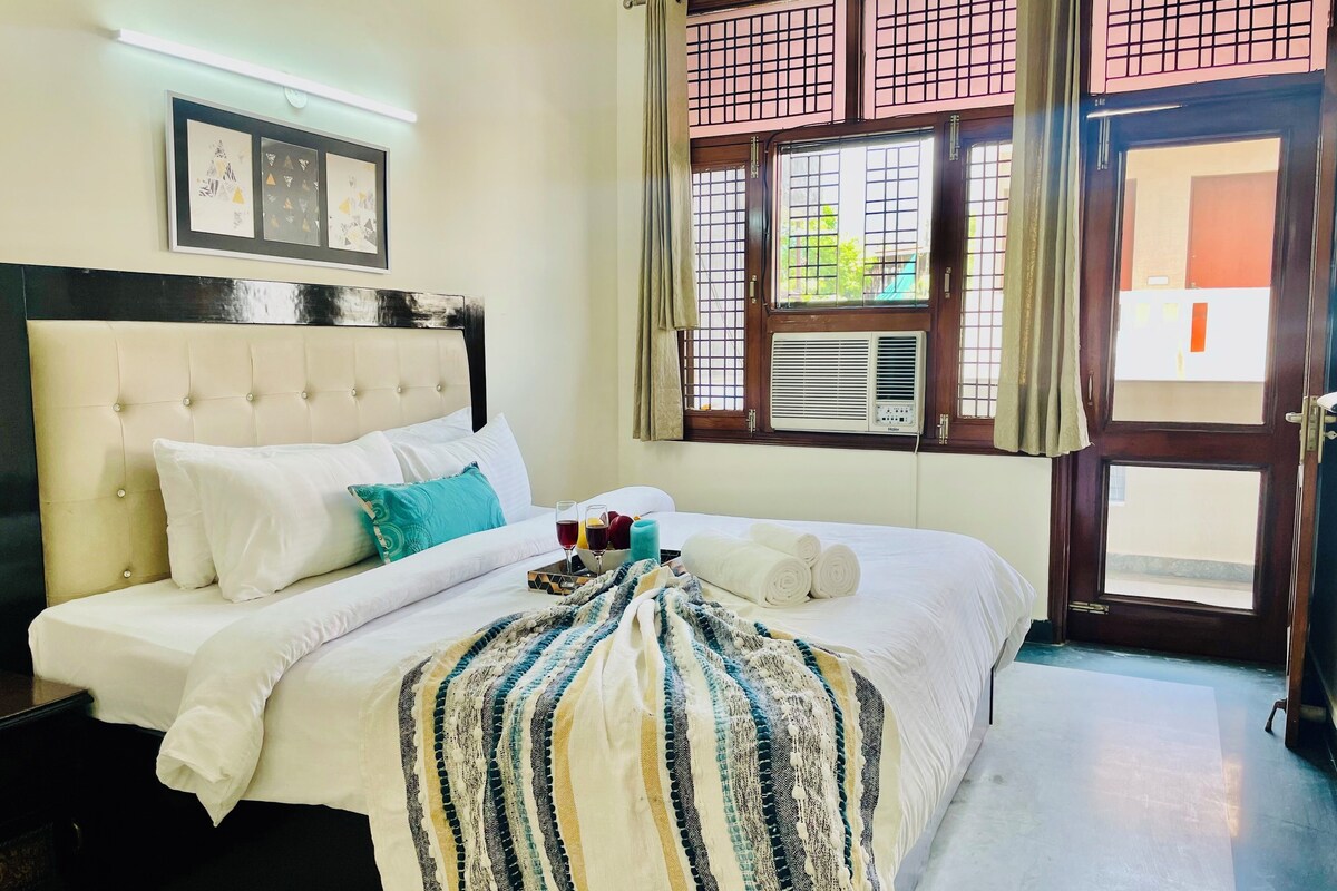 A neatly made bed with white linens, a striped blanket, and a teal pillow. There are two framed pictures on the wall above the bed.